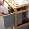 A person is placing a piece of clothing into a grey fabric basket on a bamboo shelf unit. Produktbild-Vorschau