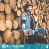 A young girl wearing a helmet and protective gear sits on the ground, leaning against a stack of logs, holding a blue hoverboard. Produktbild-Vorschau