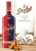 A bottle of Dooley's Toffee Cream Liqueur, two glasses with the liqueur and ice, and pieces of toffee candy are arranged on a wooden surface. Produktbild-Vorschau