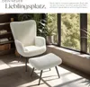 A cream-colored armchair and ottoman are placed in a cozy living room setting with plants and a large window overlooking trees. Náhled obrázku produktu