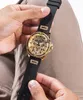 A person's hands are holding a gold and black watch with diamond-like accents. Podgląd zdjęcia produktu