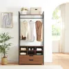 A wardrobe stand with clothes hanging on it and storage compartments below, placed in a room with a plant and artwork. Produktbild-Vorschau