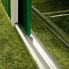 A close-up view of the bottom edge of a green sliding door for a garden shed, resting on a metal track laid on artificial grass. Produktbild-Vorschau