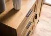 A close-up view of a wooden dresser with rattan accents and black handles, with two white vases on top. Produktbild-Vorschau