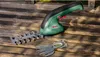 A Bosch EasyShear Akku-Strauchschere is placed on a wooden surface, with two different cutting attachments nearby. Anteprima dell’immagine prodotto