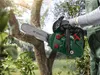 A person is using a green chainsaw to cut a tree branch outdoors. Produktbild-Vorschau