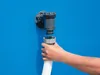 A hand is connecting a white hose to a gray filter pump attached to a blue surface. Voir les images du produit