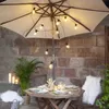 An outdoor table setting with a patio umbrella decorated with string lights. Podgląd zdjęcia produktu