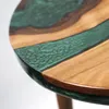 A close-up view of a round coffee table with a walnut wood top and a green epoxy resin inlay. Produktbild-Vorschau
