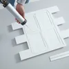 A person is applying adhesive to a white decorative panel with a caulking gun. Produktbild-Vorschau