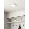 A square LED ceiling light is mounted on a white ceiling above a shelf with decorative plants and coat hooks. Voir les images du produit