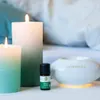 A still life arrangement of two lit candles, a small bottle of essential oil, and a white aroma diffuser with a soft yellow glow. Podgląd zdjęcia produktu