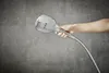 A hand holding a shower head in front of a tiled wall. Anteprima dell’immagine prodotto