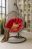 A hanging egg chair with a red cushion and a striped pillow is placed in a room with a bookshelf in the background. Produktbild-Vorschau
