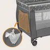 A close-up view of a side pocket on a gray travel crib, with an inset showing baby items inside the pocket. Produktbild-Vorschau