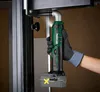 A person wearing gloves is using a cordless angle impact wrench to tighten a bolt on a metal frame. Náhled obrázku produktu