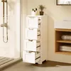 A white bathroom cabinet with four drawers is shown next to a shower stall. The top drawer is slightly open, revealing items inside. To the right, there is another storage unit with shelves. A small potted plant sits on top of the cabinet. Produktbild-Vorschau