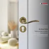 A close-up of a bronze door handle and keyhole on a white door, with a blurred interior scene in the background. Produktbild-Vorschau