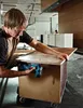 A man is using a jigsaw to cut a piece of wood in what appears to be a workshop or construction site. Produktbild-Vorschau