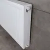 A white radiator mounted on a gray tiled wall. Produktbild-Vorschau