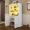 A white high-gloss display cabinet with open doors, showcasing various decorative items and storage boxes inside. The cabinet is illuminated with warm yellow LED lights. Produktbild-Vorschau