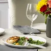A table setting with a plate of food, a wine glass, and a vase of flowers. Produktbild-Vorschau
