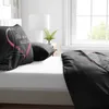 A close-up view of a bed with black bedding and a pillow featuring a pink heart design with the text "All you need is Love". Produktbild-Vorschau