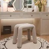 A minimalist and modern vanity area with a stool, mirror, lamp, and flowers.