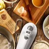 A collection of baking ingredients and tools, including a hand mixer, on a wooden surface. Produktbild-Vorschau