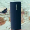 A dark blue cylindrical speaker is partially submerged in shallow water, with a rocky or sandy bottom visible beneath the water. Náhled obrázku produktu