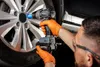 A person wearing orange gloves and safety glasses is using a cordless impact wrench to tighten a lug nut on a car wheel. Podgląd zdjęcia produktu