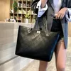 A person is holding a black quilted leather tote bag in front of a bookshelf. Náhľad obrázku produktu