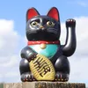 A black Maneki-neko (lucky cat) figurine sits on a wooden post against a blue sky with clouds. Produktbild-Vorschau