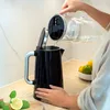 A person is pouring water from a glass pitcher into a black electric kettle. Produktbild-Vorschau