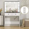 A white and black vanity table with a lighted mirror, makeup, and drawers, set against a light gray wall with a woven basket and draped fabric. Voir les images du produit