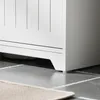 A close-up shot of the base of a white cabinet standing on a tiled floor. Produktbild-Vorschau