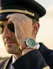A pilot wearing sunglasses and a pilot hat, adjusting his hat and showing his watch. Náhľad obrázku produktu