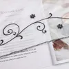 A close-up of a sheer curtain with embroidered floral and vine patterns, laid over an open book. Produktbild-Vorschau