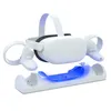 A white Oculus Quest 2 VR headset and controllers are shown resting on a white charging dock with blue LED lights. Produktbild-Vorschau
