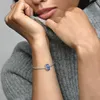 A close-up shot of a woman's wrist wearing a Pandora bracelet with a blue charm, while she is wearing a grey sweater. Produktbild-Vorschau