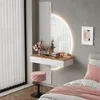 A modern bedroom vanity area with a floating white and oak desk, a round LED mirror, and a pink velvet stool. Produktbild-Vorschau