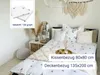 A bedroom scene with a bed made up with white bedding featuring a subtle black deer pattern, decorated with bohemian-style accessories. Produktbild-Vorschau