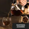 A person is pouring tea from a glass teapot into a glass cup. A jar of tea leaves is visible in the background. Produktbild-Vorschau