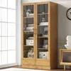 A wooden display cabinet with glass doors filled with books and decorative items, placed near a window and a wall clock. Podgląd zdjęcia produktu