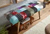 A patchwork upholstered bench is placed in a room with a brick wall and wooden floor, with a vintage suitcase underneath. Produktbild-Vorschau