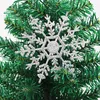 A close-up of a silver glitter snowflake ornament hanging on a green artificial Christmas tree. Produktbild-Vorschau