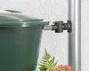 A close-up of a green rain barrel with a black connector attached to a downspout. Náhled obrázku produktu
