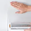 Weiße strukturierte Tapete wird an einer Wand angebracht, mit einer Hand, die sie glättet, und einer sichtbaren Rolle der Tapete Náhľad obrázku produktu