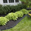 A garden bed with black plastic edging and hosta plants, with a yellow wheelbarrow filled with soil in the background. Náhled obrázku produktu