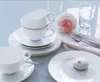 A table setting with white porcelain dishes, cups, saucers, a flower, and a meringue. Produktbild-Vorschau